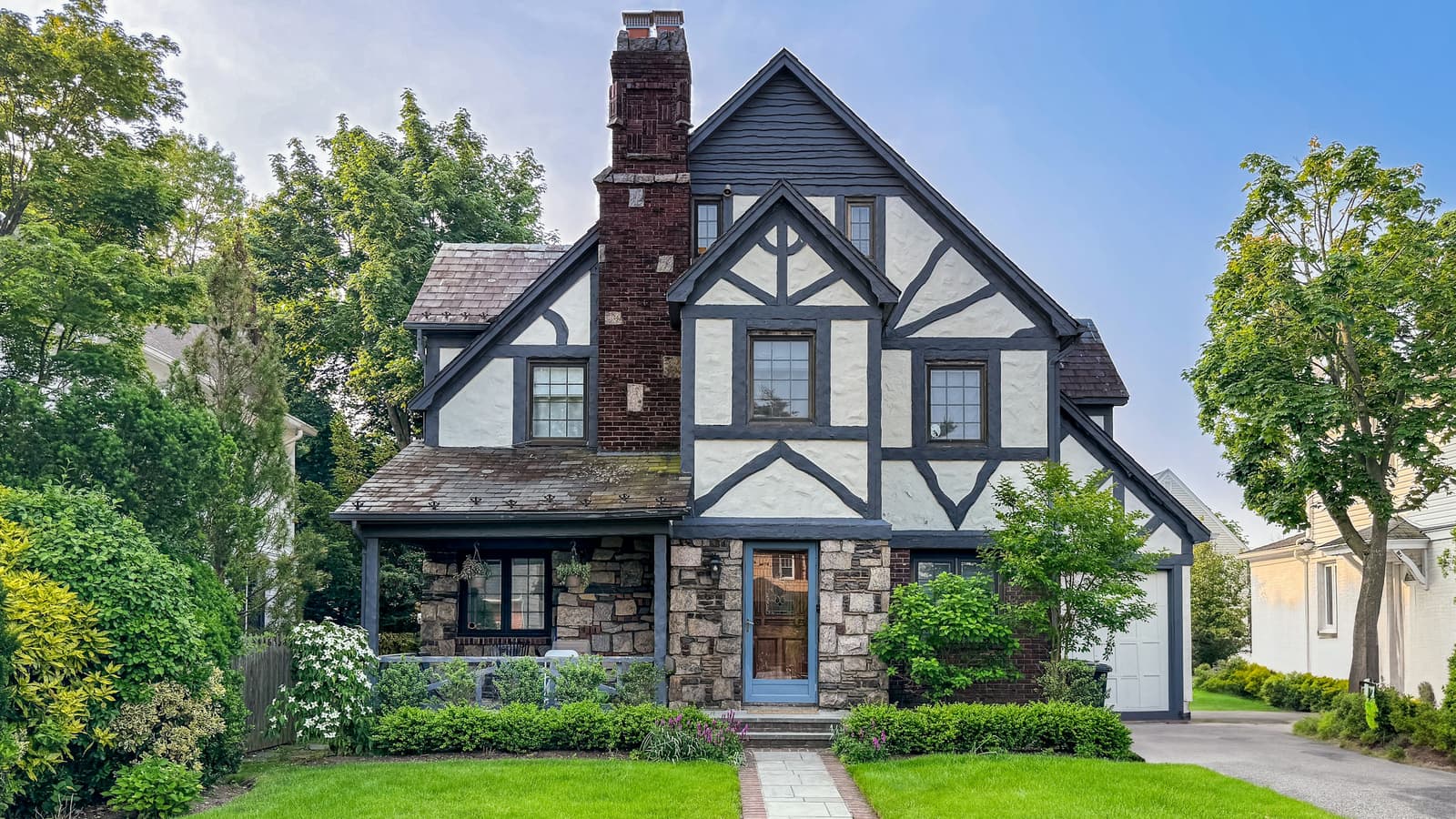 Tudor-style house with a steep roof, neatly trimmed green lawns and hedges, and a brick walkway to the front door